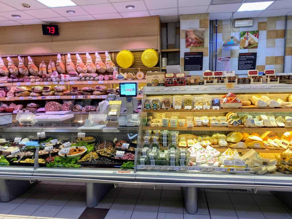 The deli section of an Italian grocery store.  You can see meats on the left in the back - legs of prosciutto, sausages, salami.  In the foreground, you can see oil-preserved products like olives and sundried tomatoes.  On the right you can see a display of cheeses.