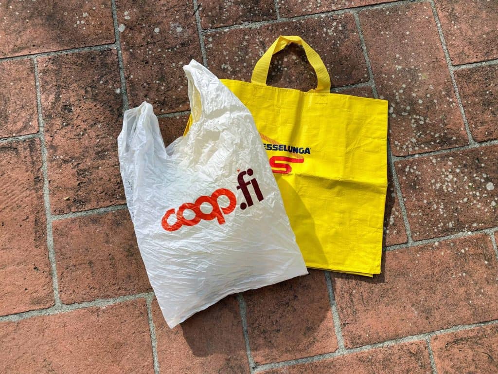 Grocery bags lying on a terracotta floor.  They are from Italian grocery stores - a white plastic bag from Coop and a yellow reusable bag from Esselunga.