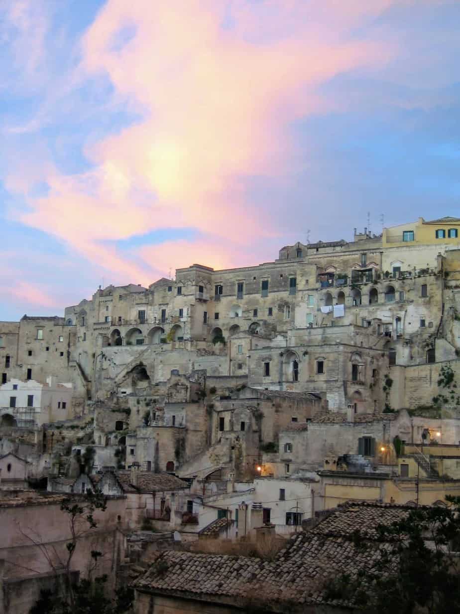 Sunset over the buildings of Matera Italy.  The sky is light pink and light blue and lavender. 