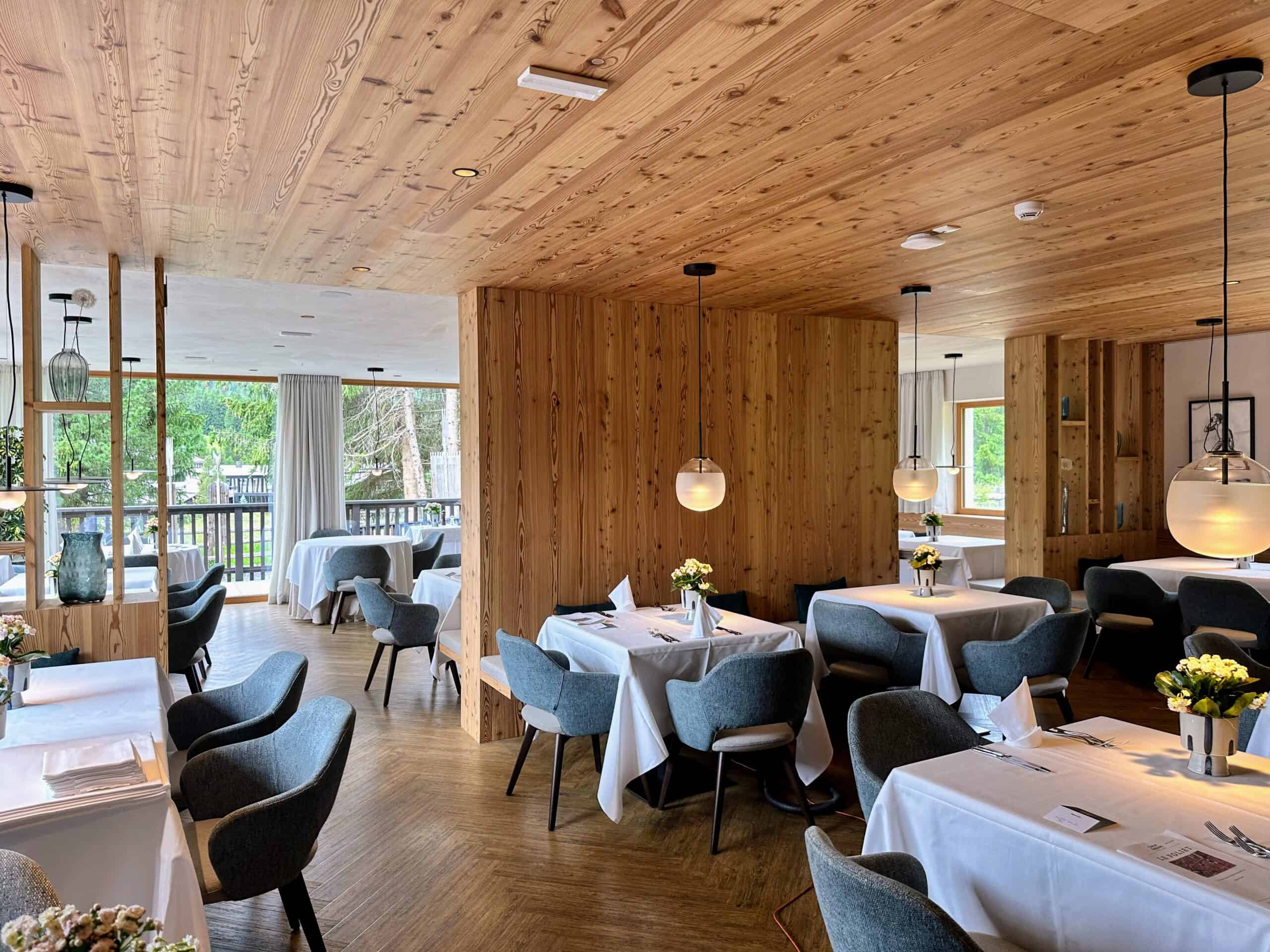 Inside empty dining room. Walls, ceiling and floor all pine wood. Tables have white tablecloths.