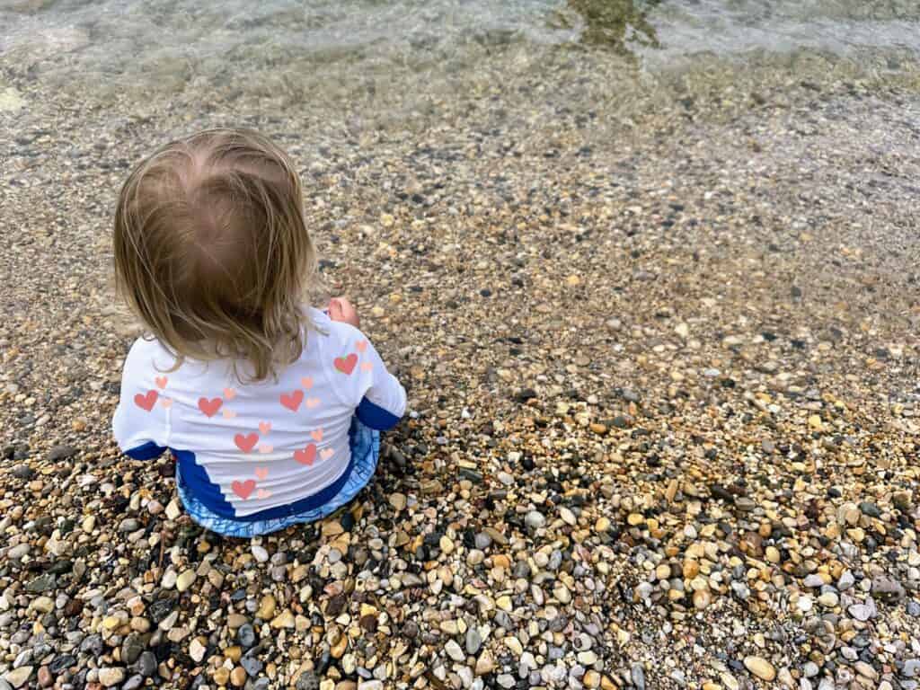 Baby sitting on edge of lake in Italy. There are small stones.