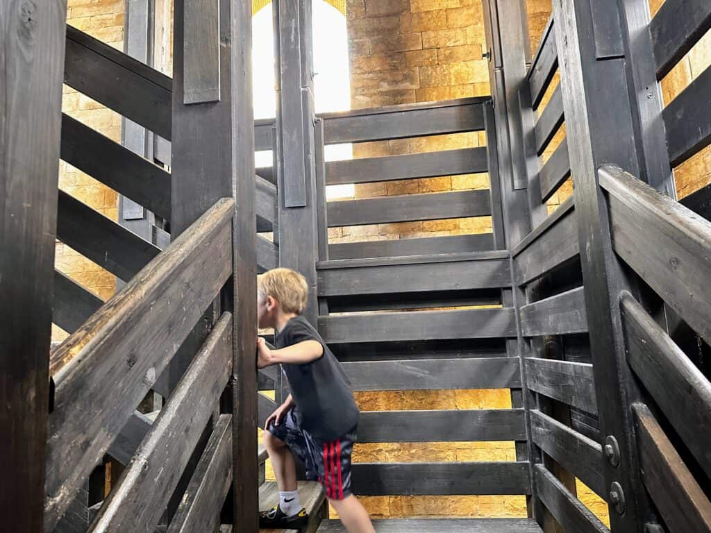 Boy walks up wooden staircase in a stone building (the bell tower of Trani, Puglia).