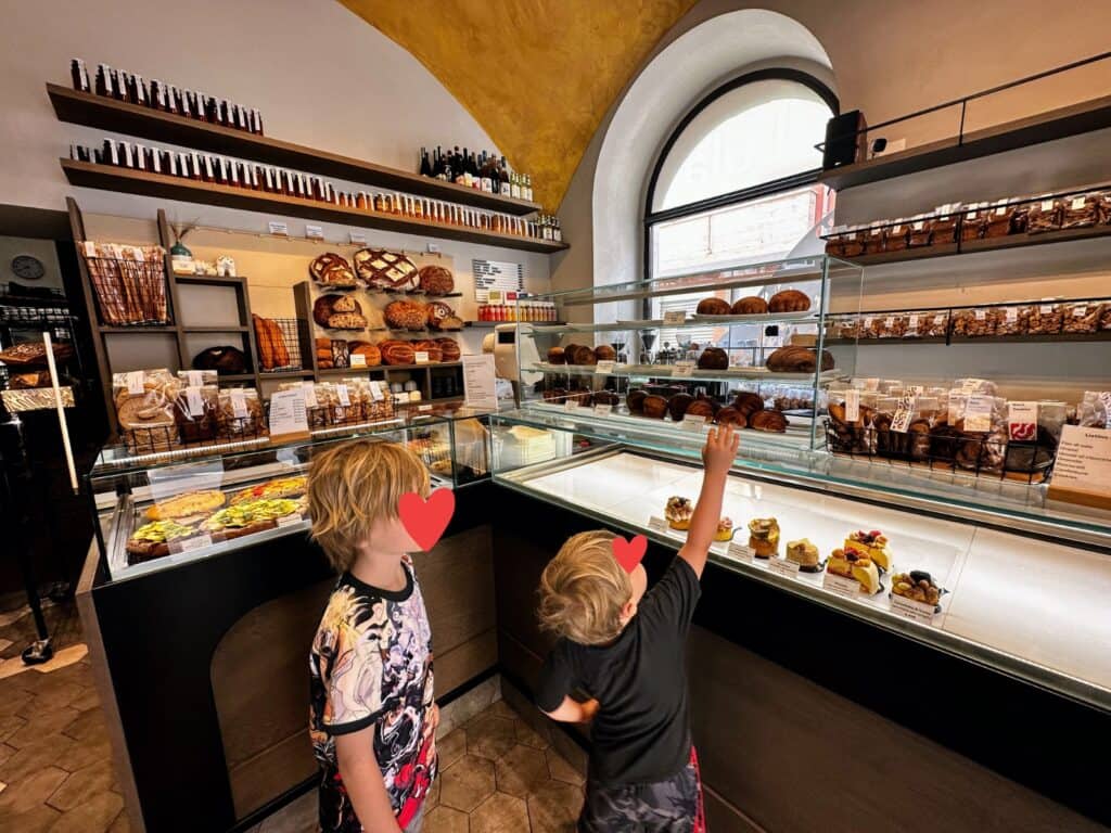Boys look at pastries for sale at Lula bakery in Trani, Italy. The glass display cases have sweet treats and focaccia and there are other breads and products on the walls.