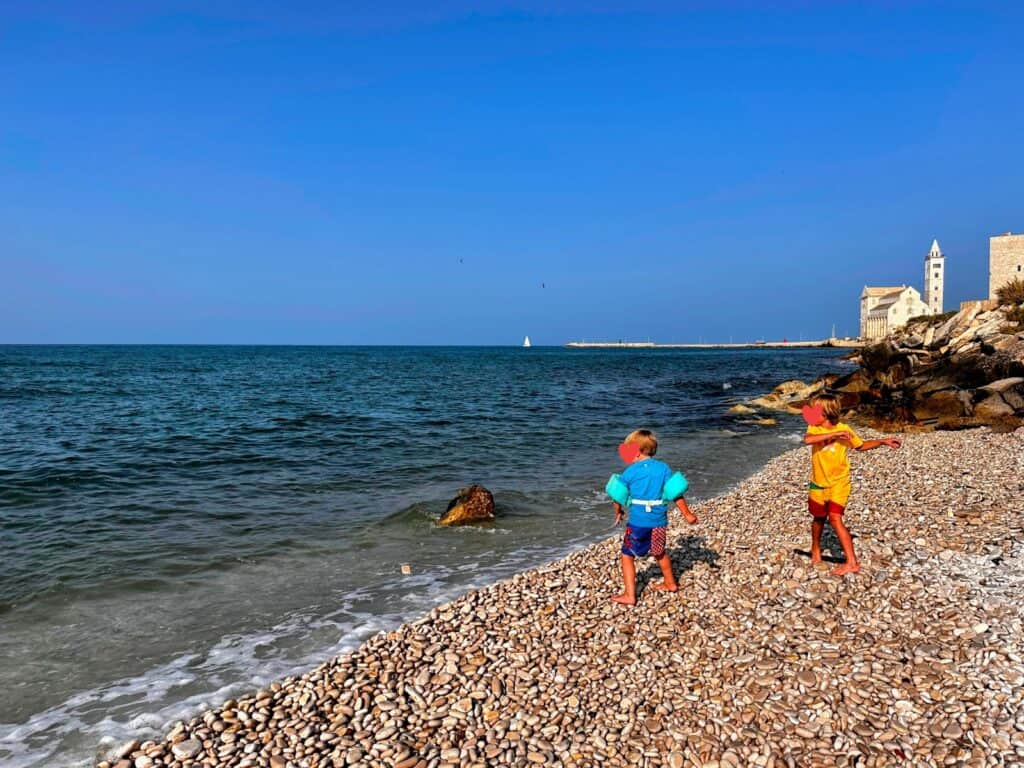 Two boys skip stones into the sea in Trani, Italy. Cathedral in the background overlooking the sea.