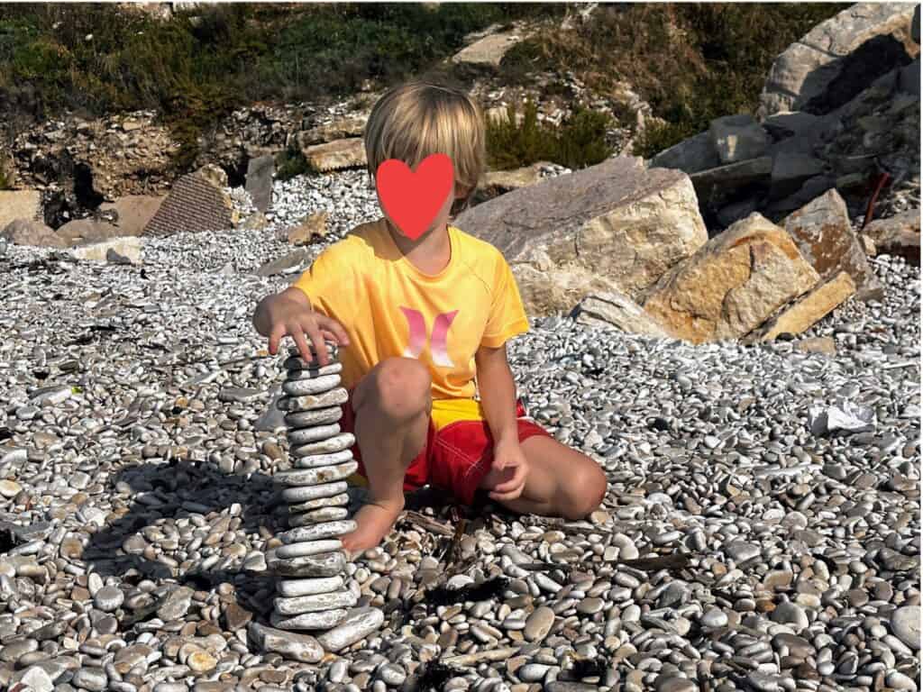 Boy stacks flat rocks into a tower on a stone beach in Trani, Italy.