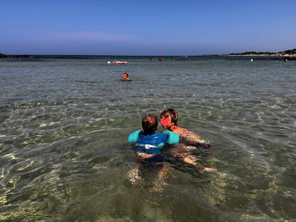 Boys swimming in shallow water at Torre Guaceto beach in Puglia, Italy. People standing and swimming further out.