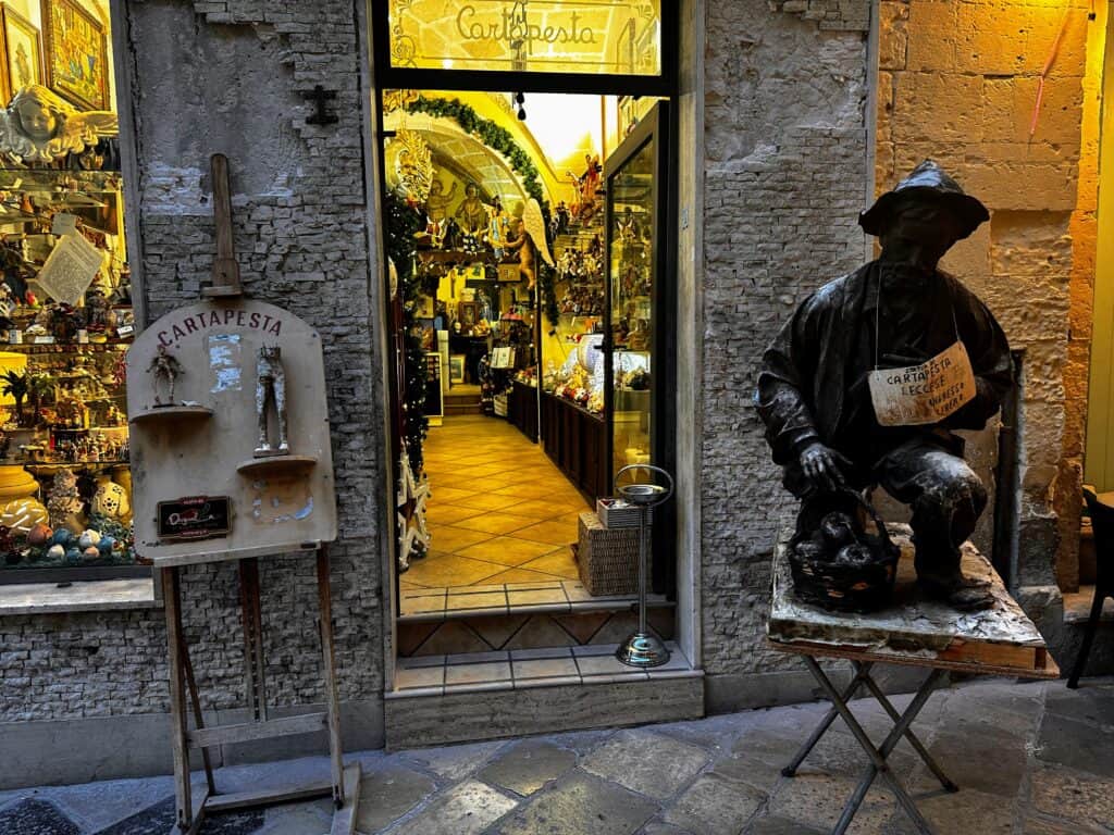 Papier-maché statue of man on display in front of a cartapesta shop in Lecce, Puglia. Other papier-maché gifts, trinkets, and decorations are on display in the store.