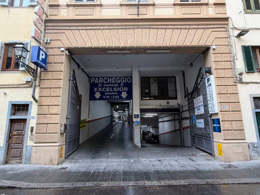Entrance to the Garage Excelsior in Florence, Italy. There are two entrances - the one on the right leads slightly downhill into the garage and the one on the left leads up. The building is stone and multi-story. No one is on the street in front of the entrance.