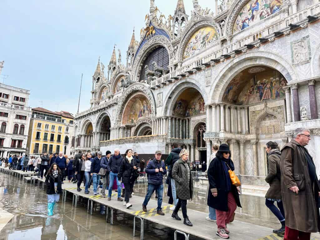 Tourists walk on raised wooden platforms in front of the Basilica di San Marco in Venice. The square is flooded.