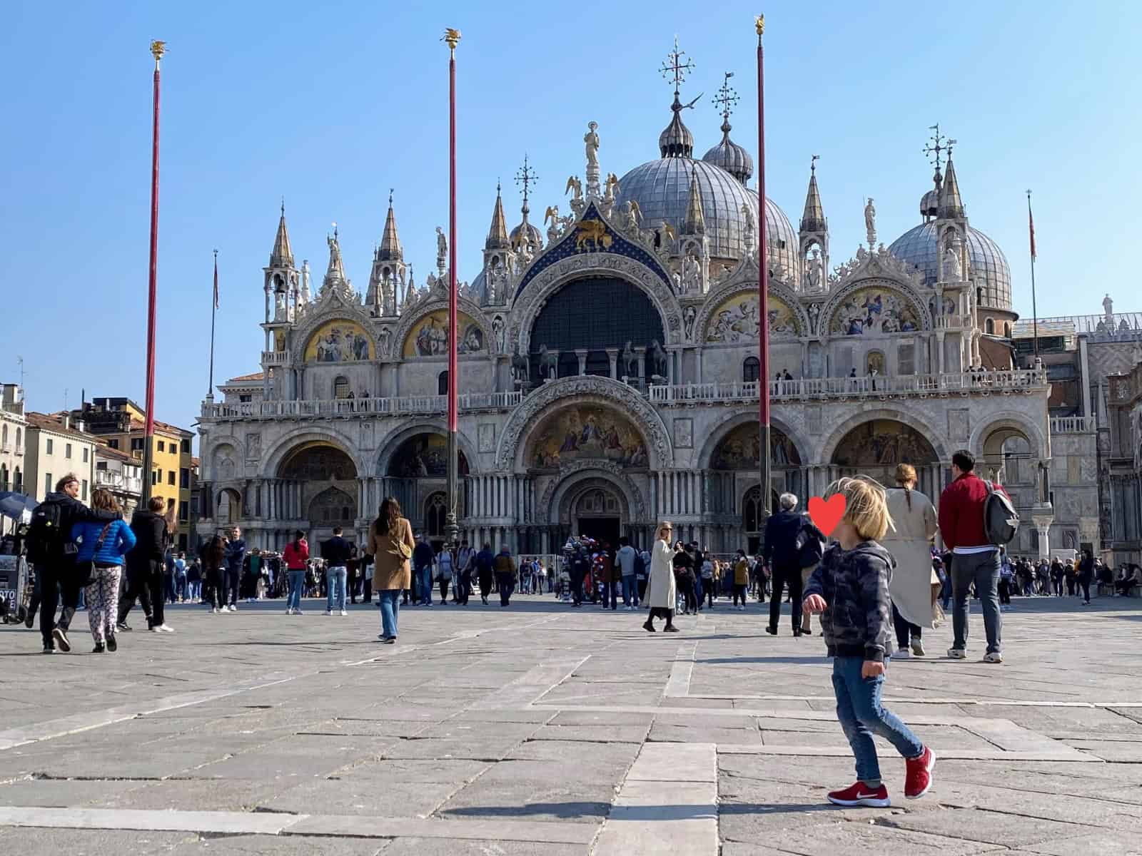 Boy stands in Piazza San Marco in Venice, in front of the Basilica. Other walk around the piazza.