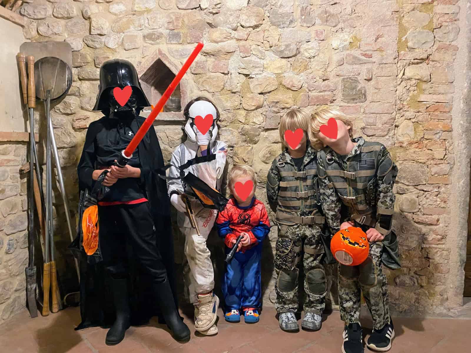 Boys in Halloween costumes stand next to a stone wall in Italy.