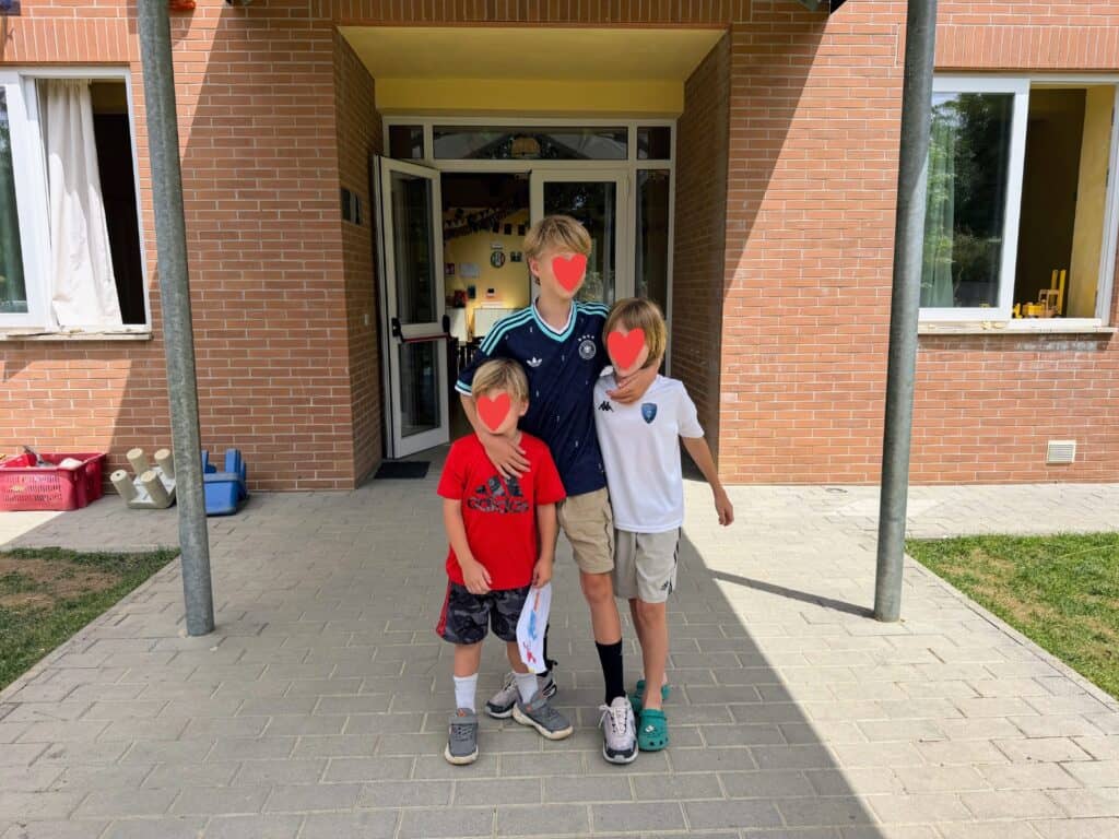 Three boys stand in front of the entrance to a school in Italy.