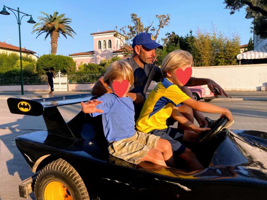 Boys and father on a bat man go kart in Forte dei Marmi, Italy. Residential area in background.