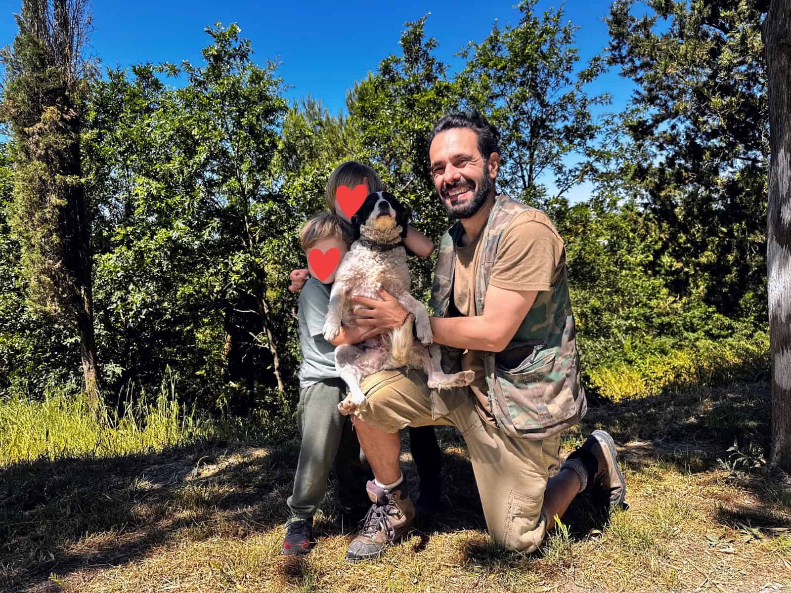 Truffle hunter holds his dog next to two boys. The woods are in the background.