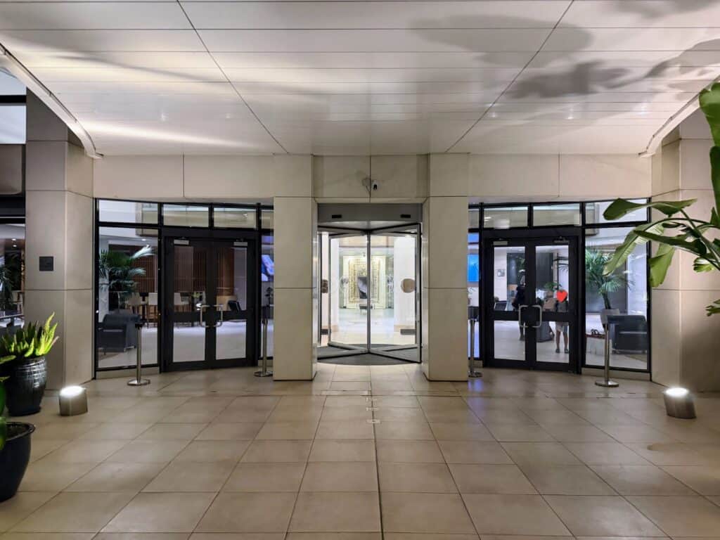 Front entrance at Precise House Mantegna Rome. Revolving glass door in center and two large glass doorways on either side. Light colored floors and ceiling.