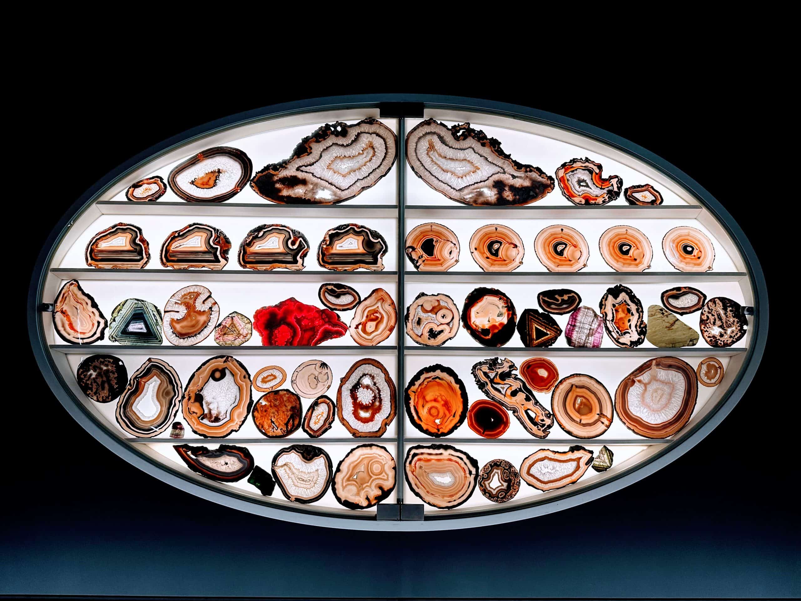A display of cross-sections of gemstones, backlit, in an oval setting. The display is placed against a black background.