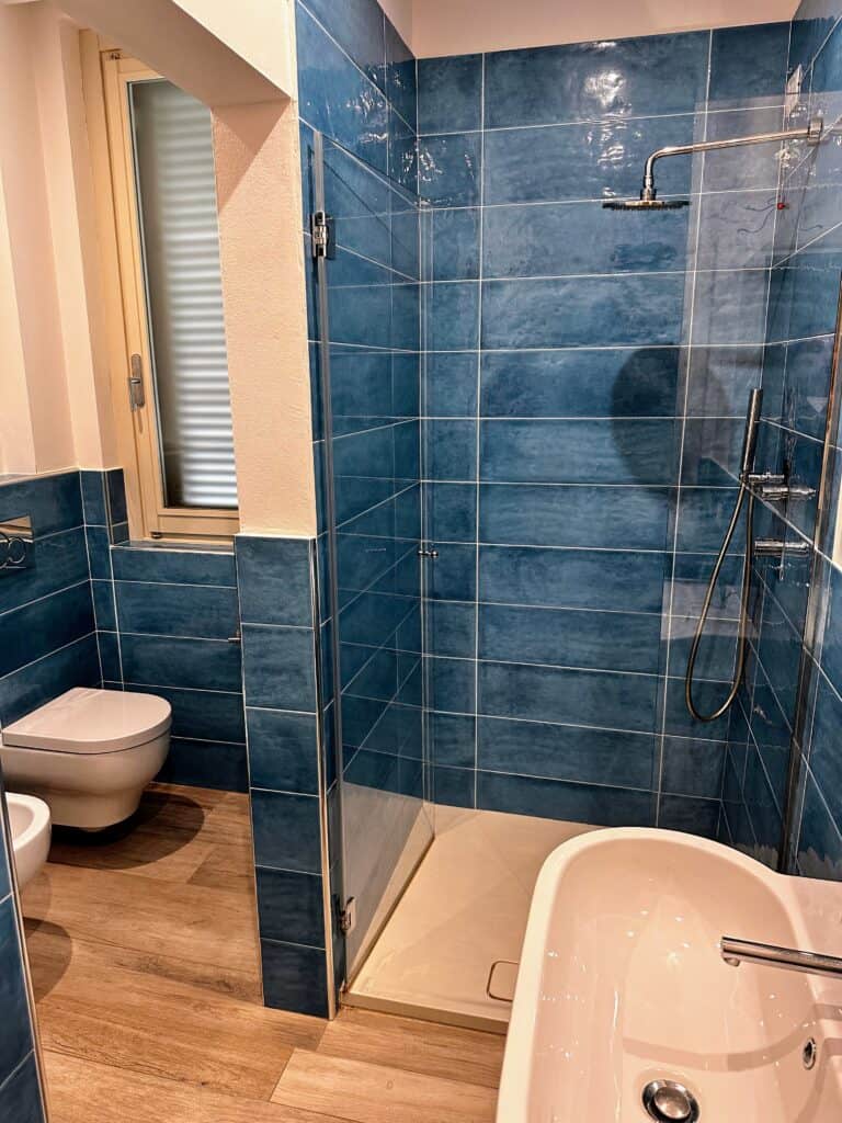 Bathroom in Italy with shower, sink, toilet, and bidet. Tile is blue.