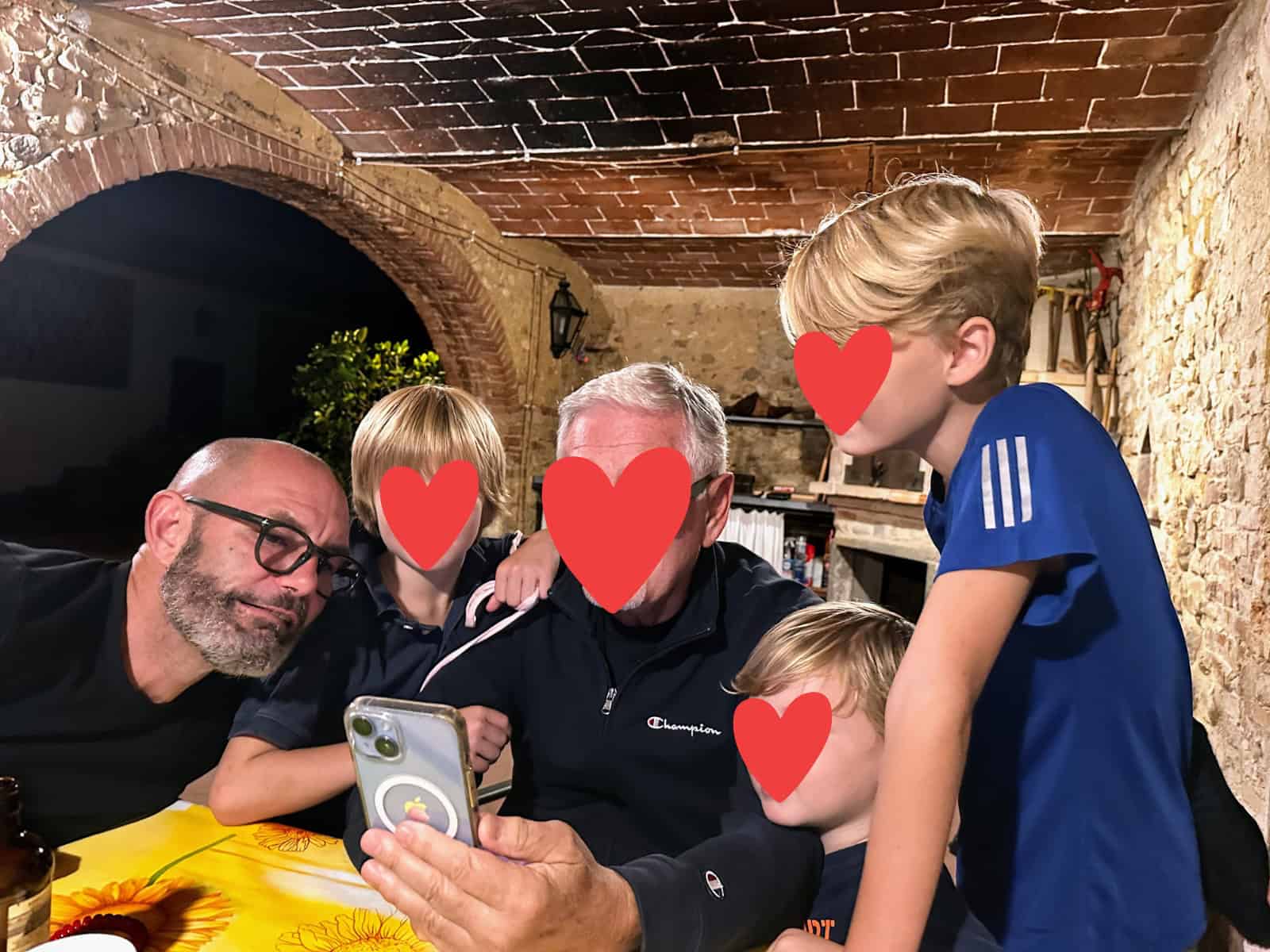 Group of Italian adults and children sit at table and look at mobile phone.