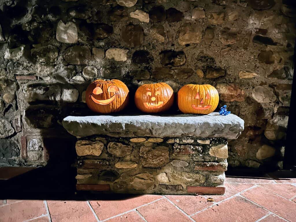 Three pumpkins are carved and lit up and sitting on a stone bench in Italy.