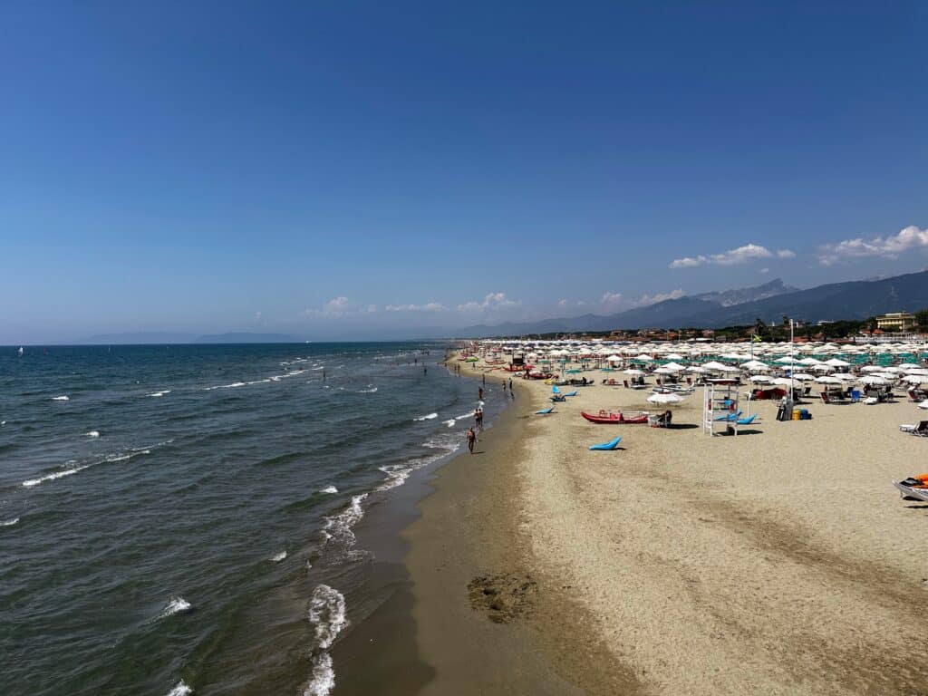 Beach and sea at Lido di Camaiore in Tuscany. Umbrellas on the beach and there are a few people wading in the water.