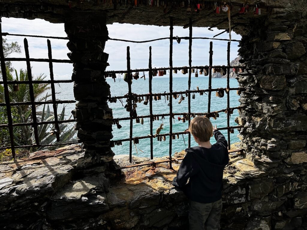 Boy looks at padlocks on iron bars next to the sea in the Cinque Terre, Italy.
