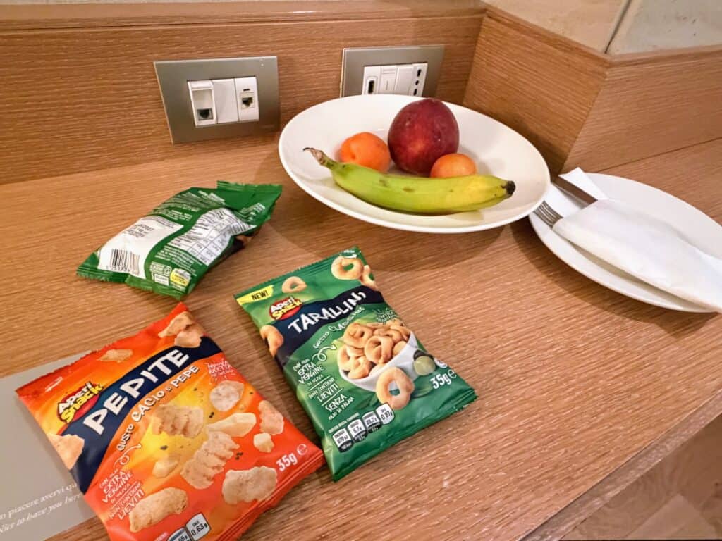 Small packs of crackers and taralli and a plate with fruit on a desk at Precise House Mantegna Rome.