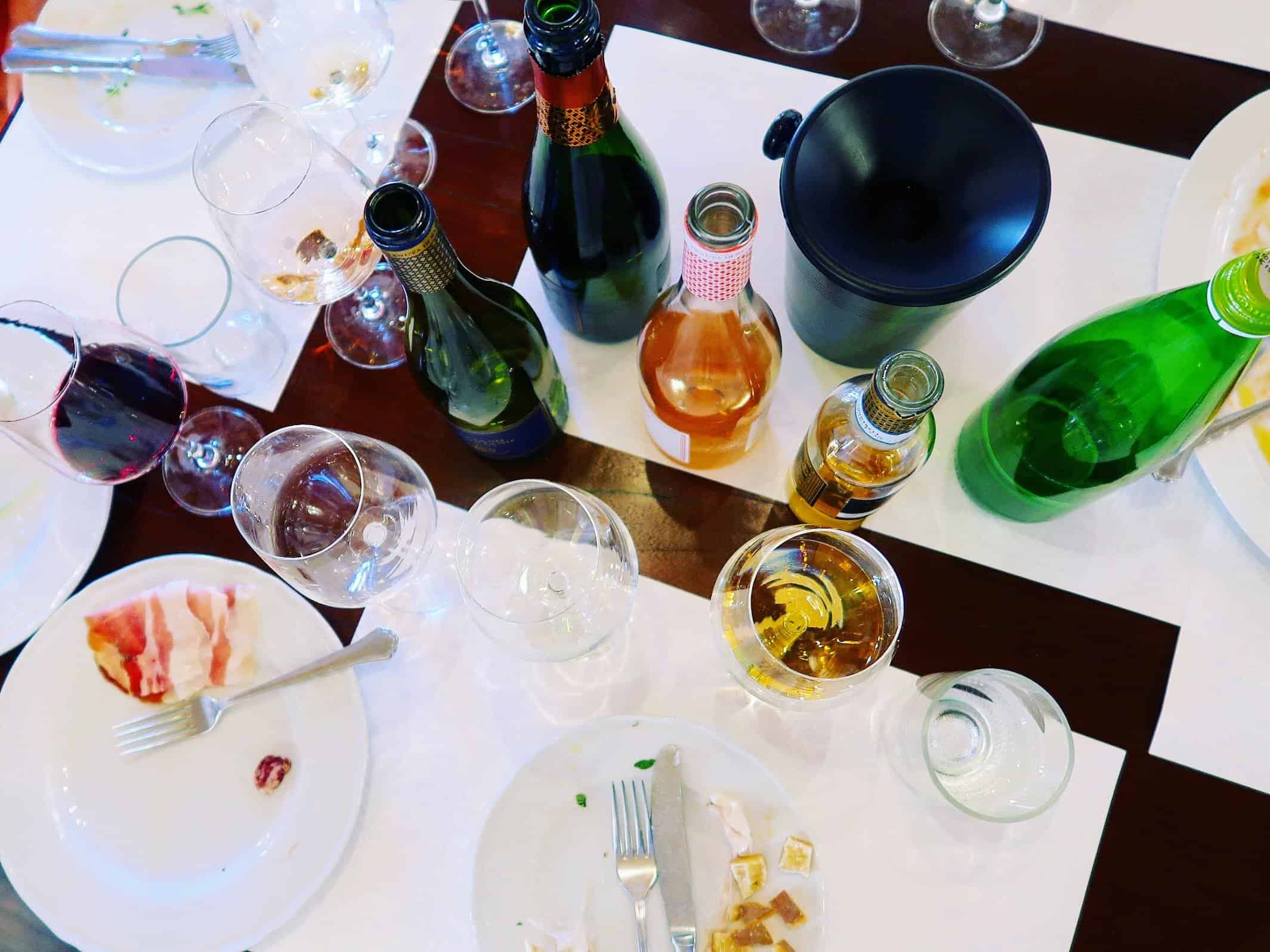 Wine glasses and bottles on a table in Italy. Plates on table too but the food has been eaten.