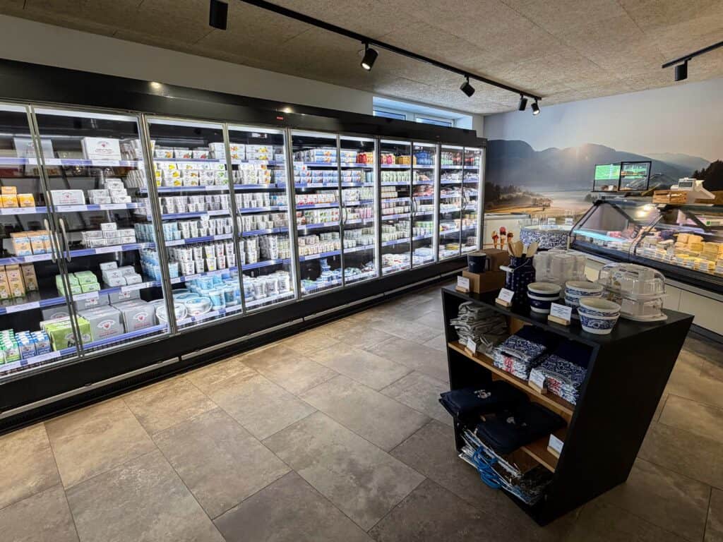 Refrigerated area inside the Sterzing-Vipiteno dairy factory in Italy. Yogurts, milk, butter, and kefir on the left. Cheeses behind a glass display on left and small shelves with kitchen utensils and products in the middle of the floor.