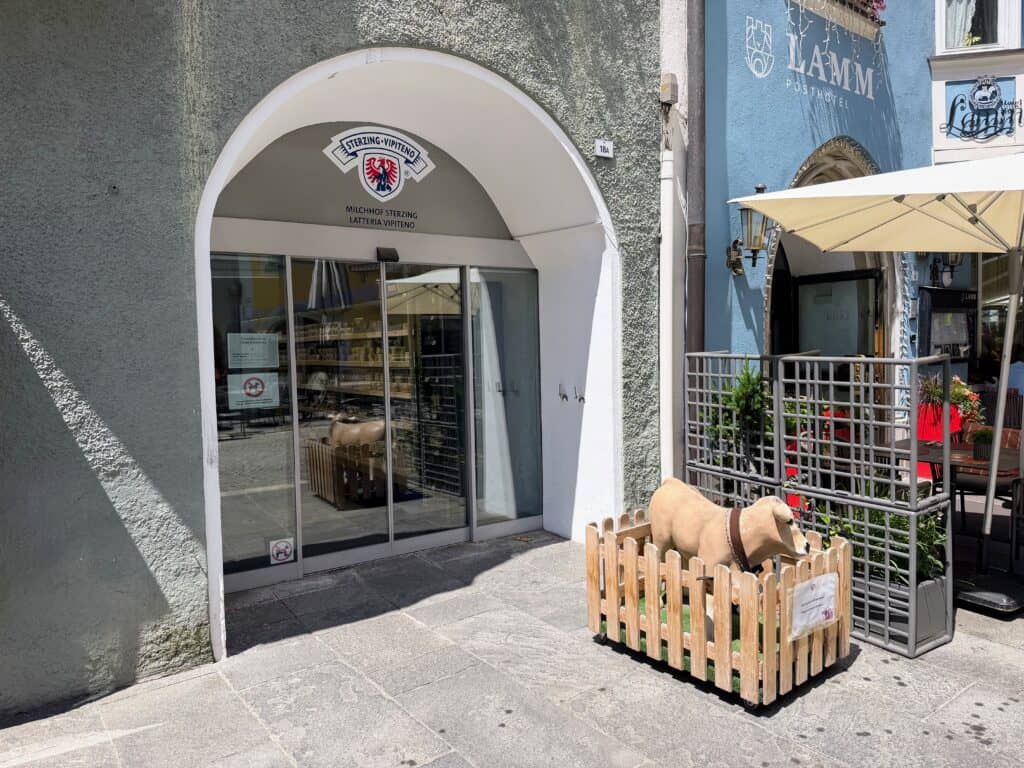 Entrance to the Sterzing-Vipiteno shop in the center of Vipiteno. Small cow figure in wooden fenced area in front of the shop.