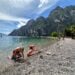 Boys playing on shore of pebbly beach with mountains in the background in Riva del Garda on Lake Garda in Italy.